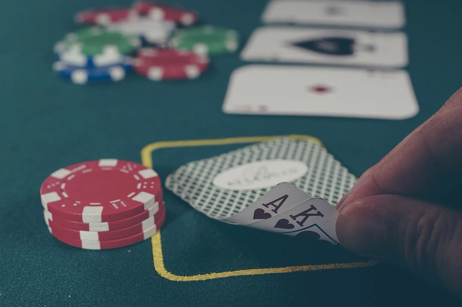 Jetons et cartes sur le tapis vert d’une table de jeu, une main soulève un as et un roi